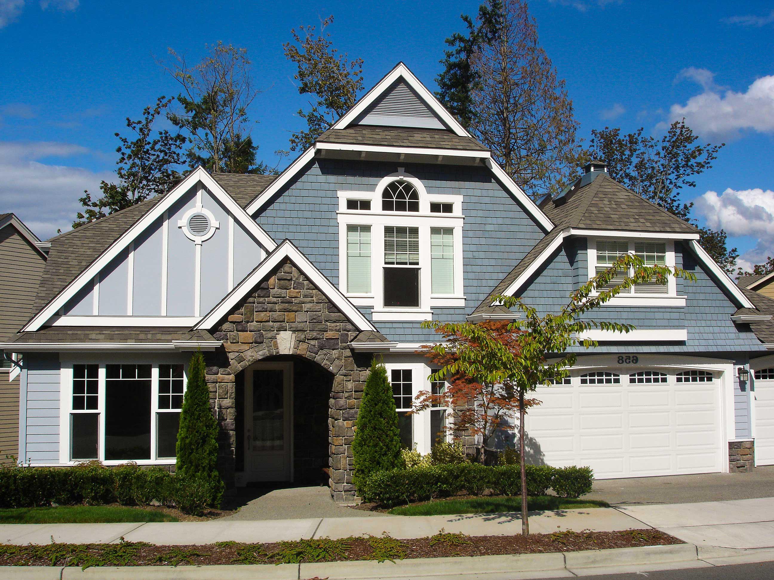House plan exterior: Two-story home with arched stone entry, multiple gables, dormers, and a side-facing garage.