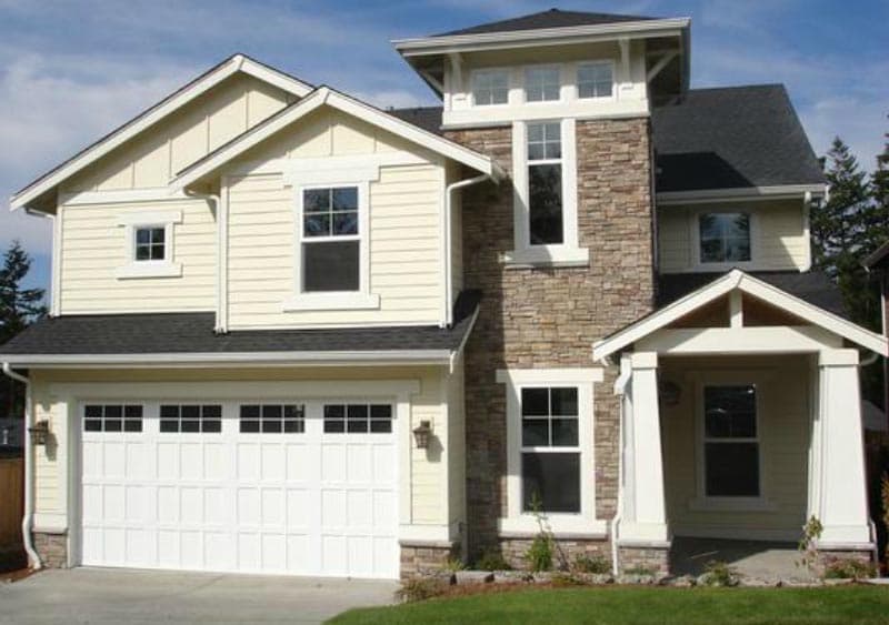 Two-story house plan exterior with stone accent tower, covered porch, and multi-pane garage door.