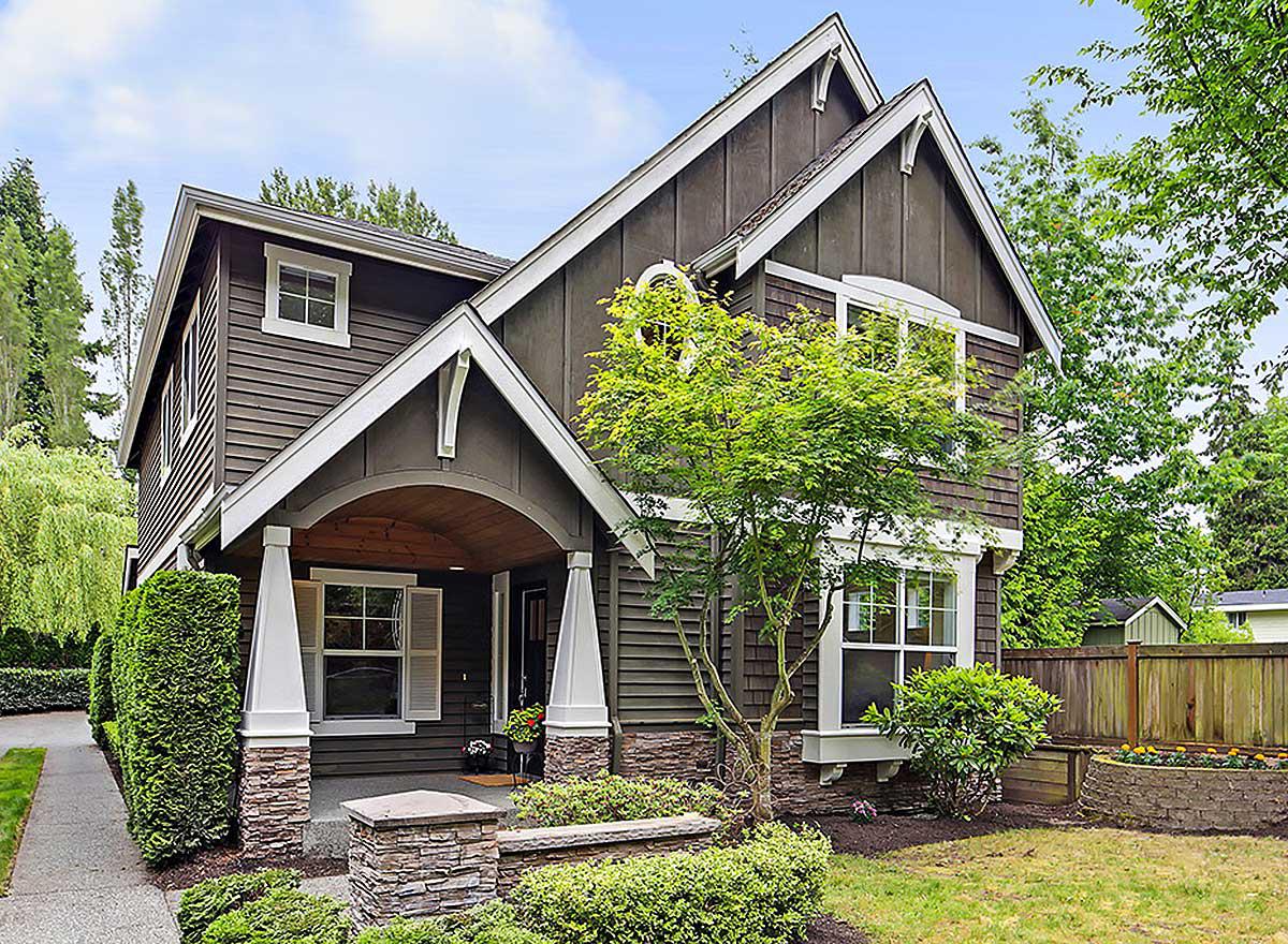 House plan exterior of two-story home with arched covered porch, stone accents, board and batten siding, and prominent gables.