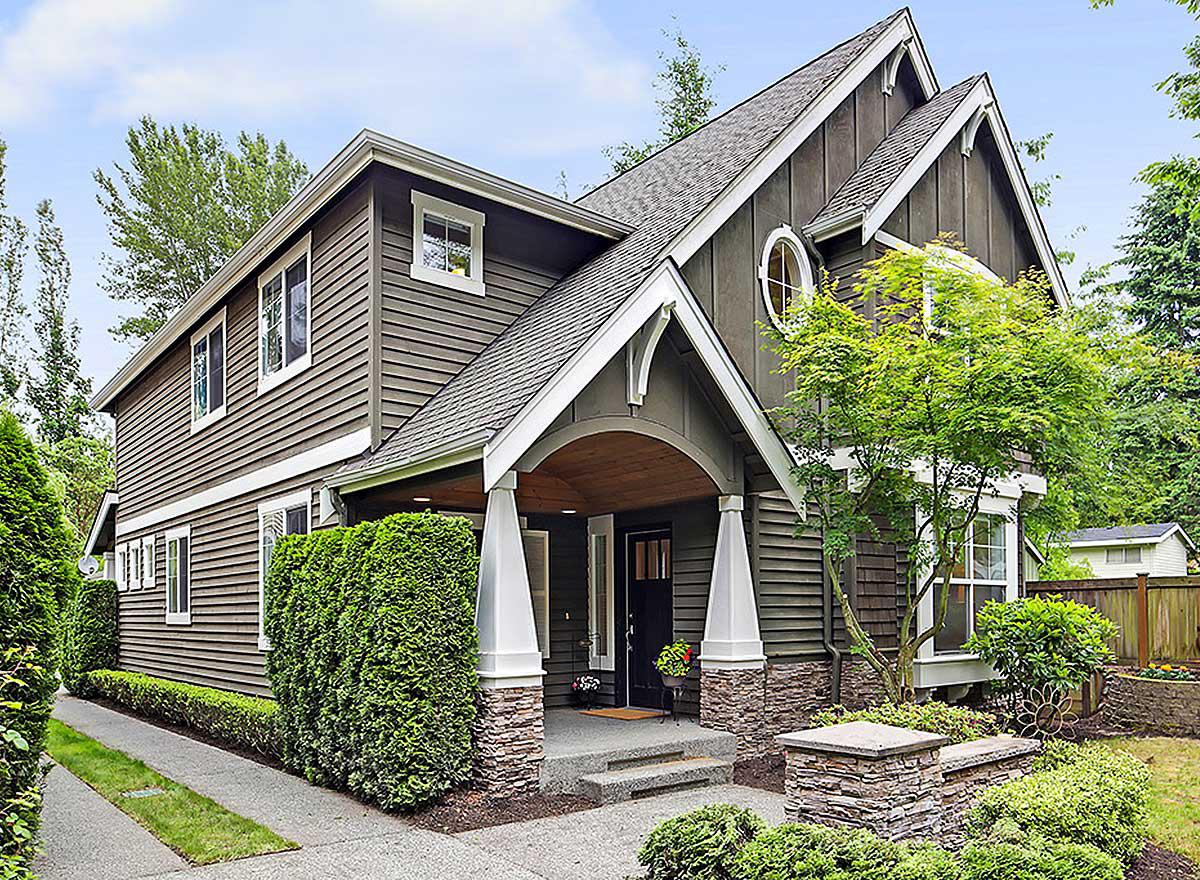 House plan exterior: Two-story home with covered porch, stone accents, gables, and a circular dormer window.