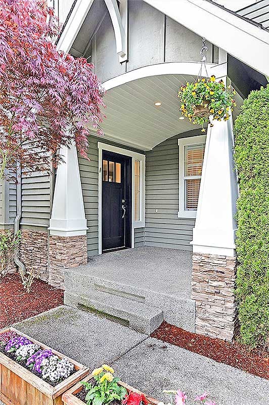 House plan exterior shows a covered porch with stacked stone accents and decorative brackets. Features a dark front door.