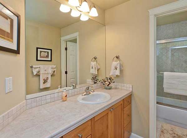 Bathroom vanity with wood cabinets, granite countertop, and sink. Mirror reflects door and bathtub with glass enclosure.