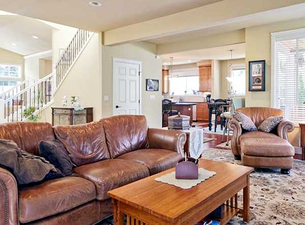 Living room with leather sofas, staircase, and kitchen visible. Open layout.