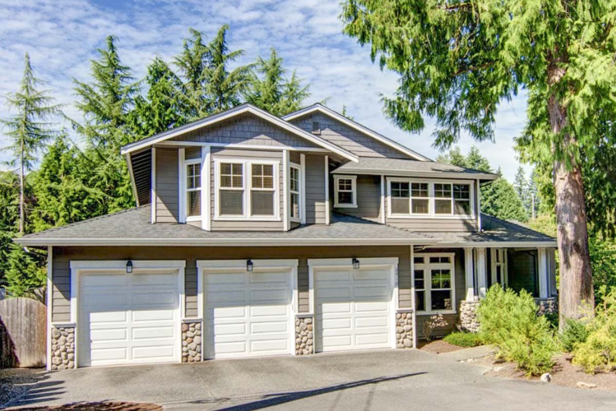 House plan exterior: Two-story home with three-car garage, bay windows, gables, and stone accents.