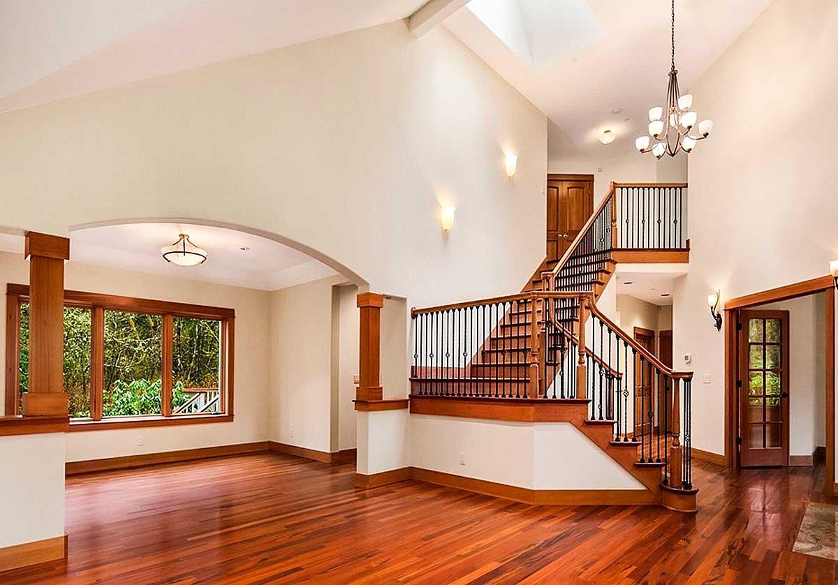 Interior view of a grand staircase with wooden treads and black spindles, flanked by large windows and an open archway.