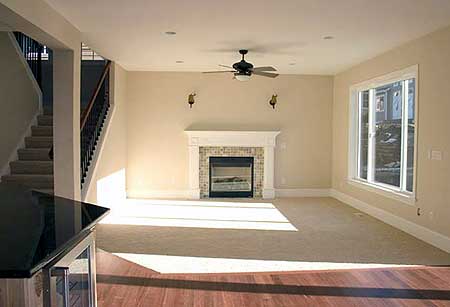 Interior view of living room with fireplace, ceiling fan, large window, and staircase.