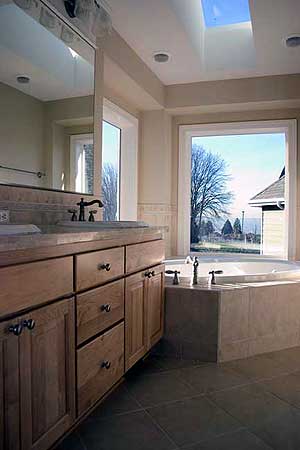 Spacious bathroom featuring a double vanity with wood cabinets, a soaking tub, and skylights.