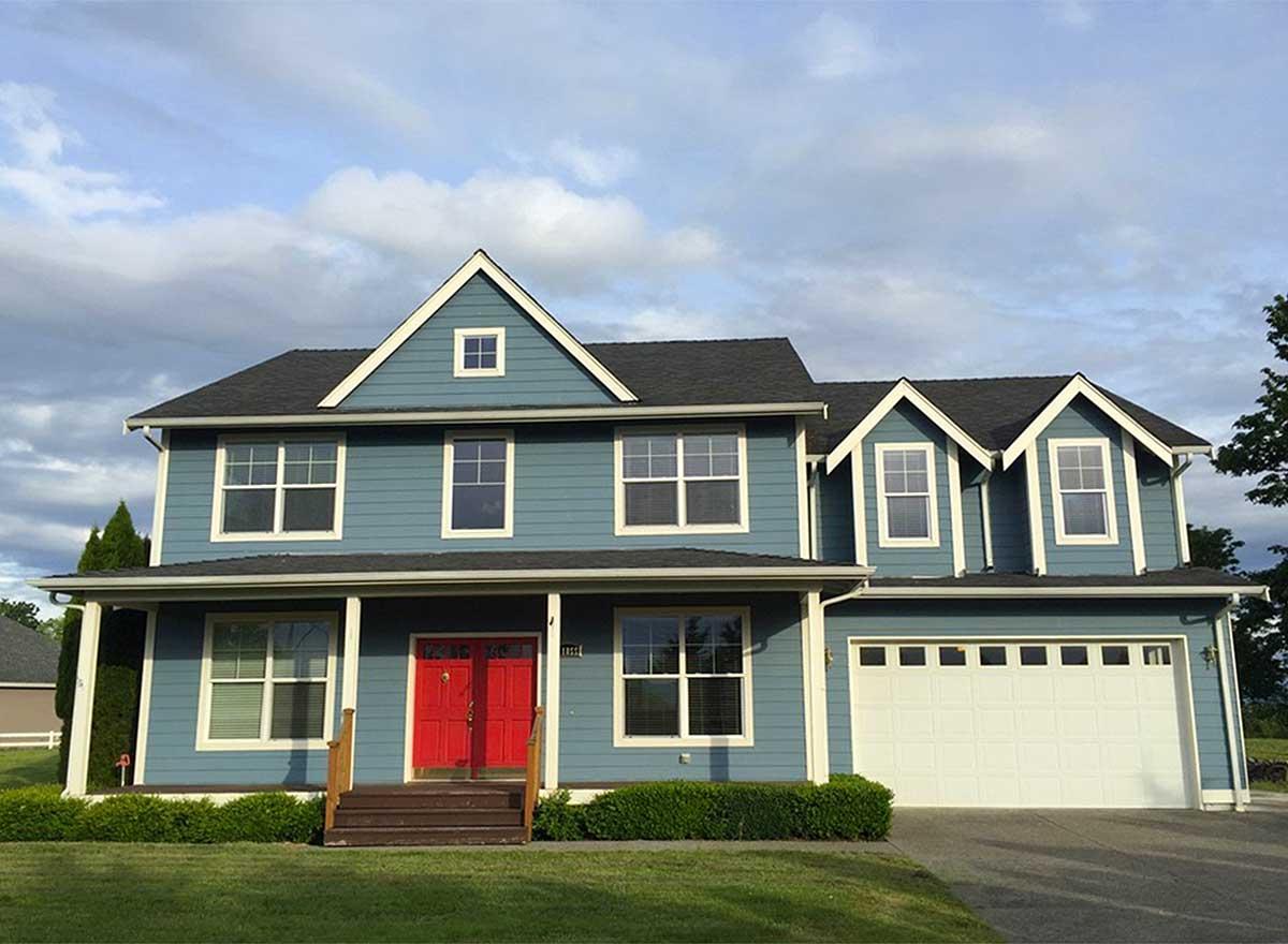 Two-story house plan exterior with a covered porch, gabled dormers, and a large attached garage. Blue siding.
