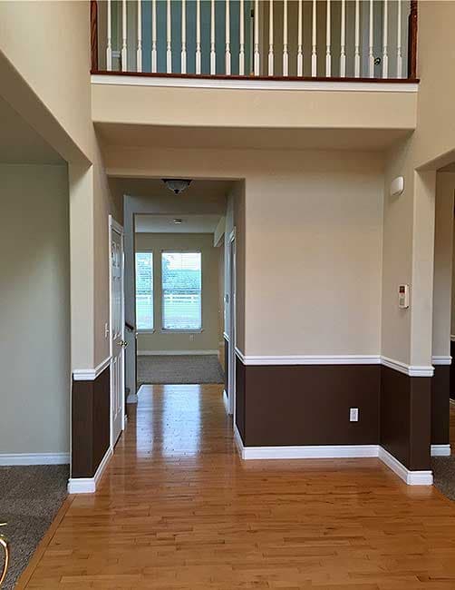 Interior view of home entry with hardwood floors, dual-toned walls, and open second-story railing.