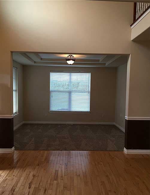 Interior view showing an open doorway to a room with carpet, a large window, and a tray ceiling.