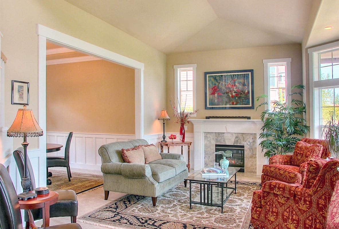 Living room with a fireplace, vaulted ceiling, and an opening to a dining area. Features two sofas, armchairs, and a glass coffee table.