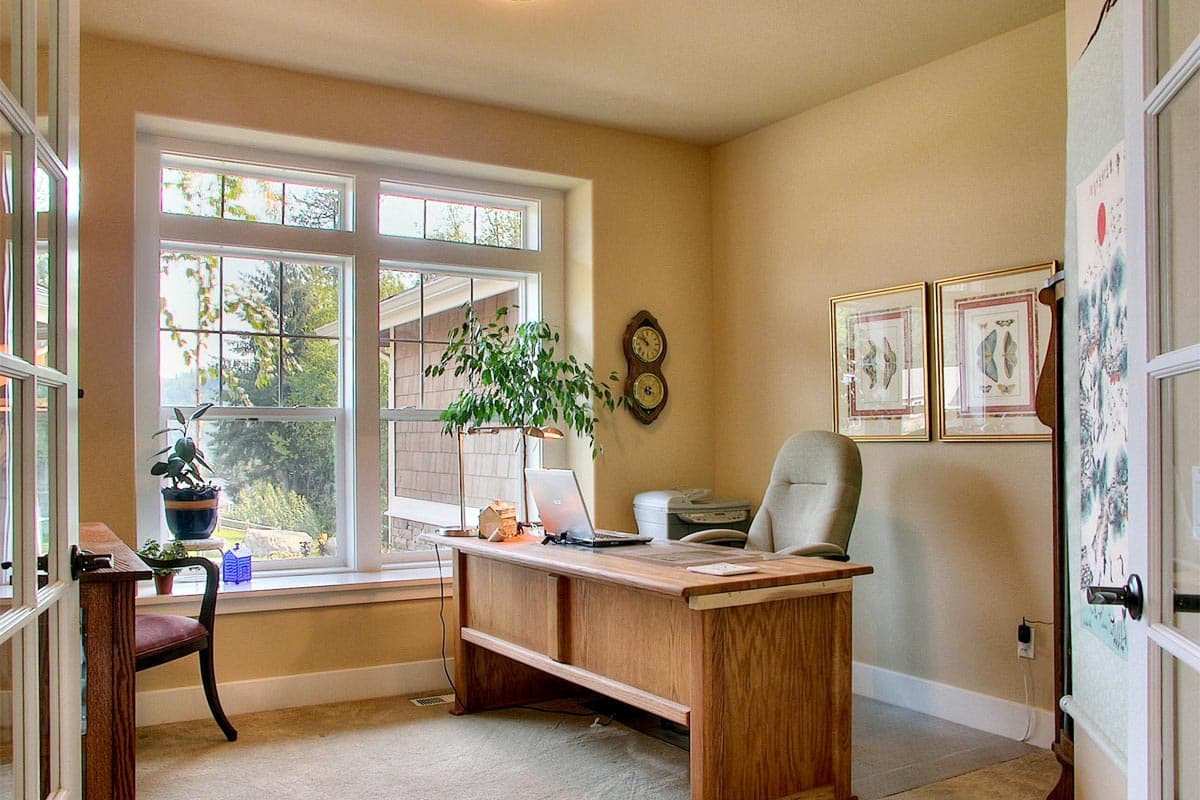 Home office with large window, wooden desk with laptop and printer, and chair.