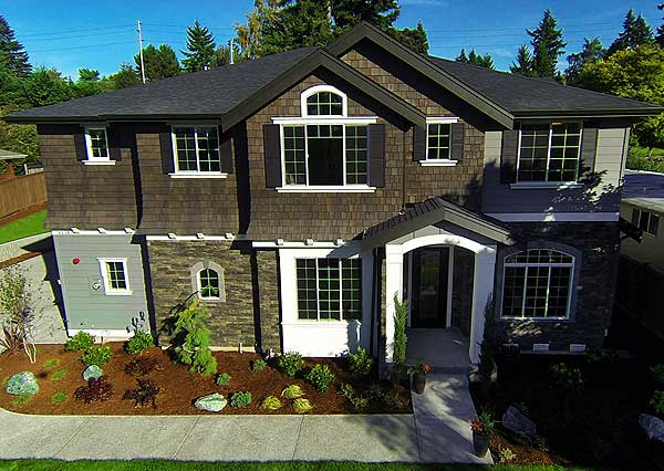 Two-story house plan exterior with shingle siding, stone accents, multiple gables, arched dormer, and covered entry.