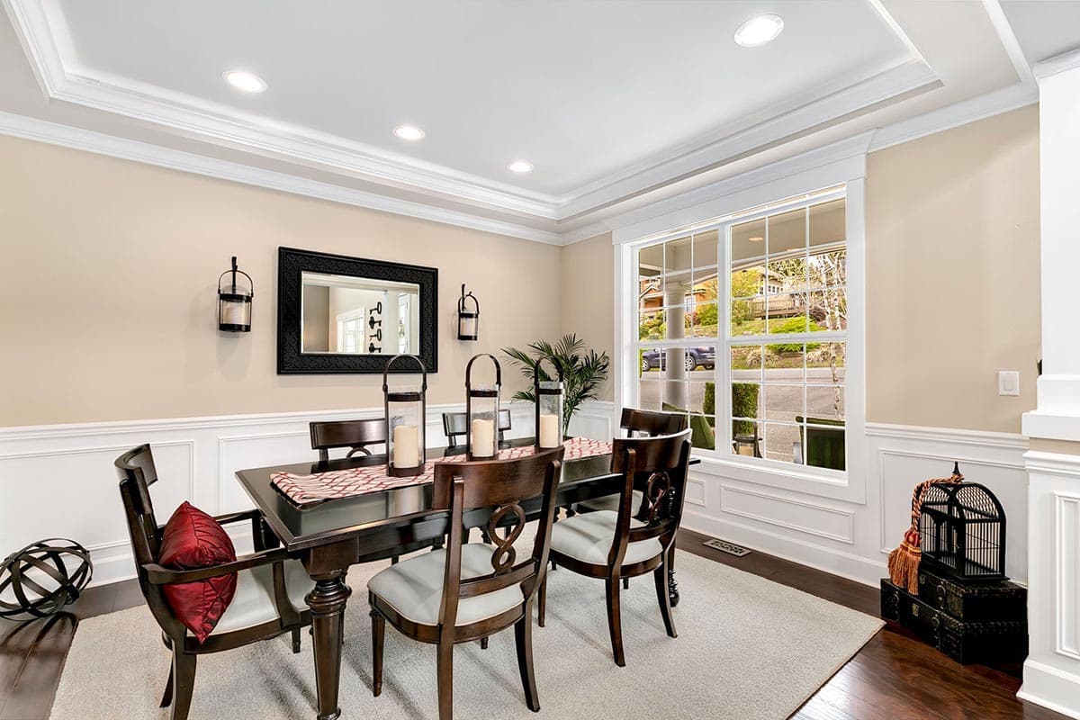 Dining room with coffered ceiling, dark wood table and chairs, large gridded window, and wainscoting.