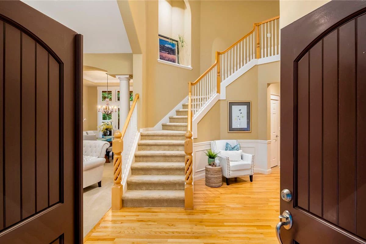Interior view of a foyer with an open staircase, wood floors, and a living area visible beyond.