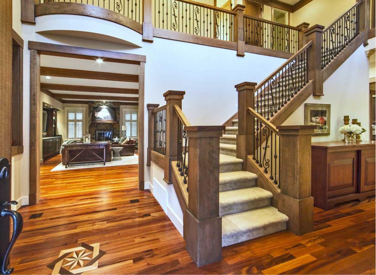 Interior view of a house entryway with a carpeted staircase, wood railings, and an opening to a living room with a fireplace.
