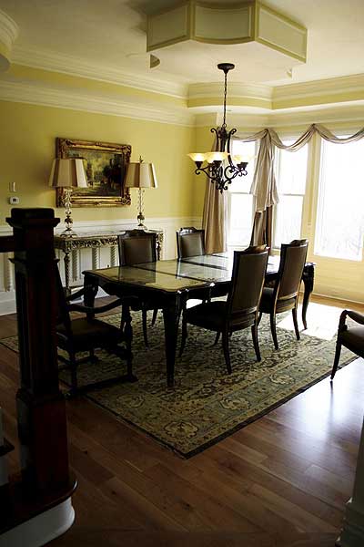 Dining room with dark wood table, chairs, patterned rug, chandelier, and large bay windows.