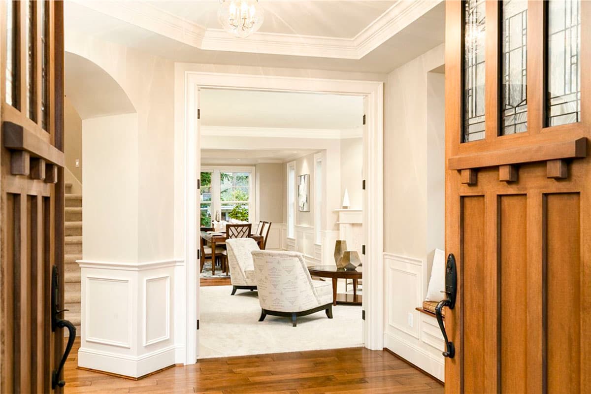 Interior view of a house entrance with wood doors, wainscoting, staircase, and view into living and dining areas.