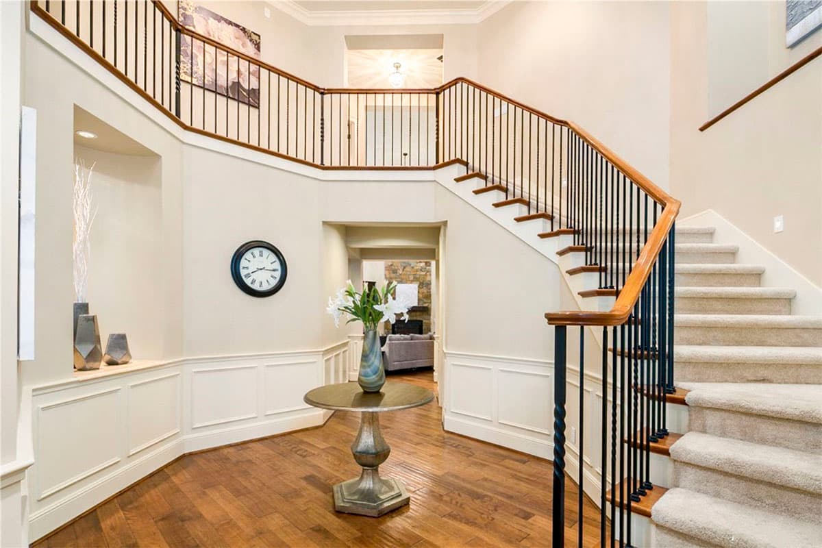 Interior view of a foyer with a curved staircase, black metal balusters, wood handrail, and paneled wainscoting.