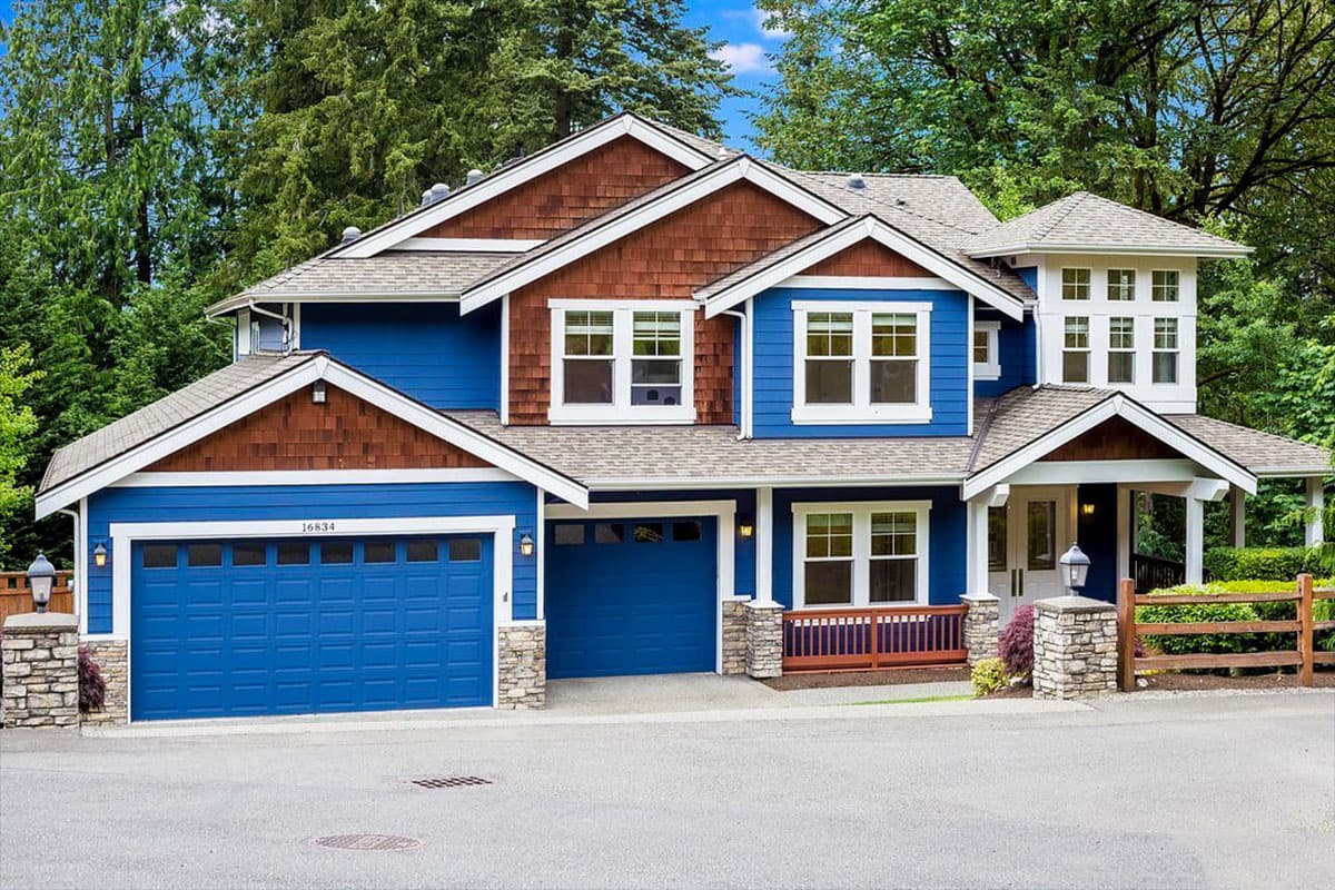 Two-story house plan exterior with blue siding, brown shingle accents, a covered porch, and a two-car garage.