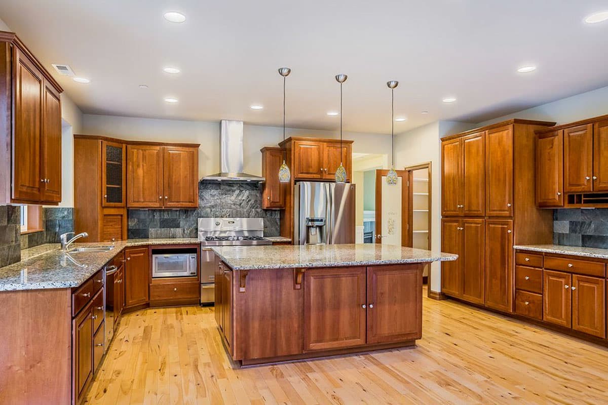 Kitchen with a central island, stainless steel appliances, granite countertops, ample wood cabinetry, and pendant lighting.