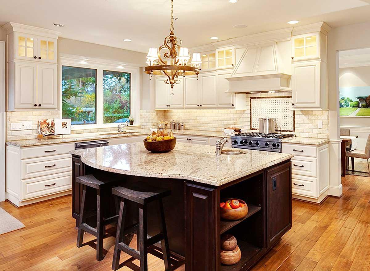 Kitchen interior featuring a large granite island with seating, white cabinets, subway tile backsplash, and stainless steel appliances.