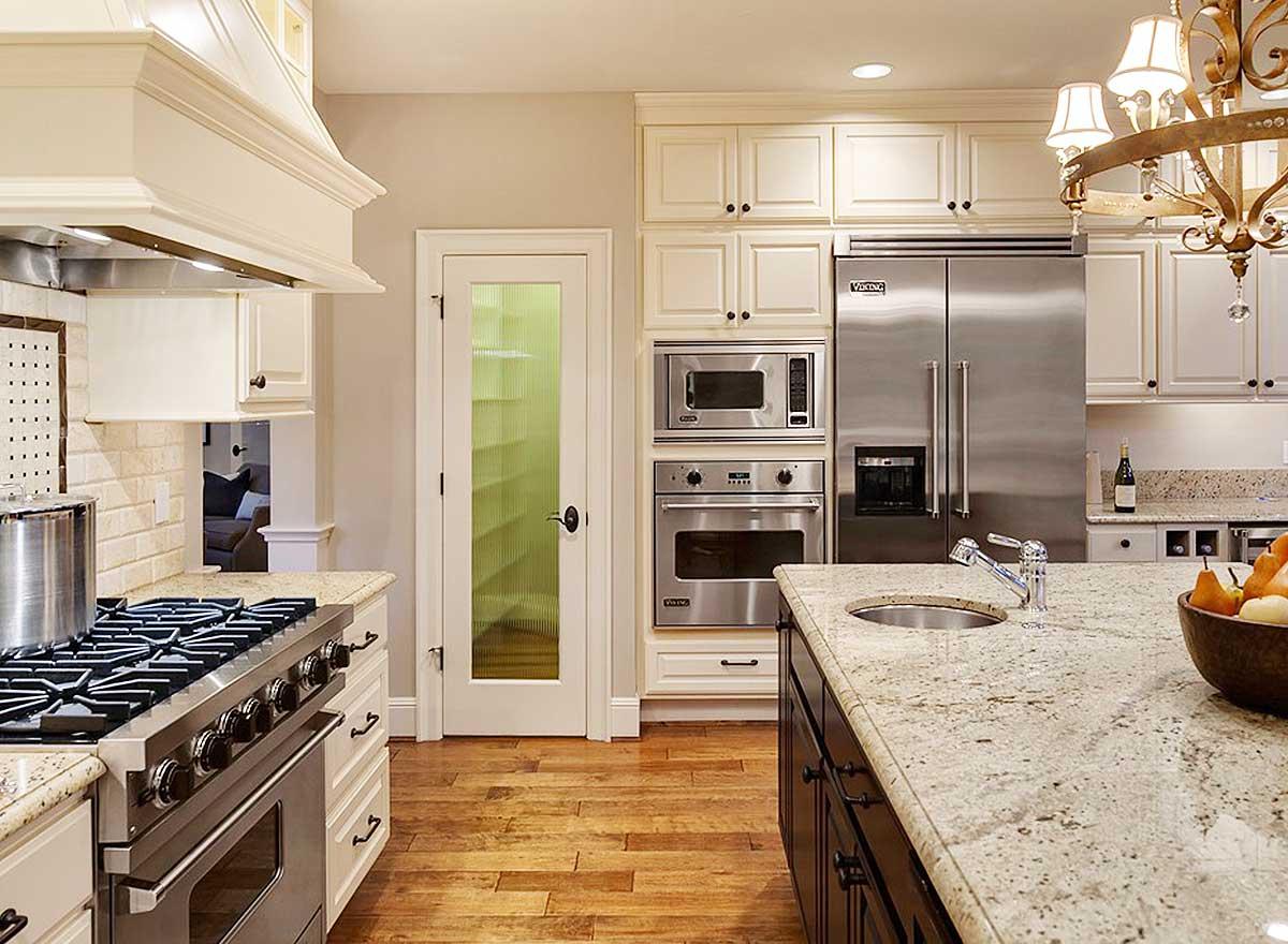 Kitchen with stainless steel Viking appliances, granite countertops, white cabinetry, a glass-paneled pantry door, and hardwood flooring.