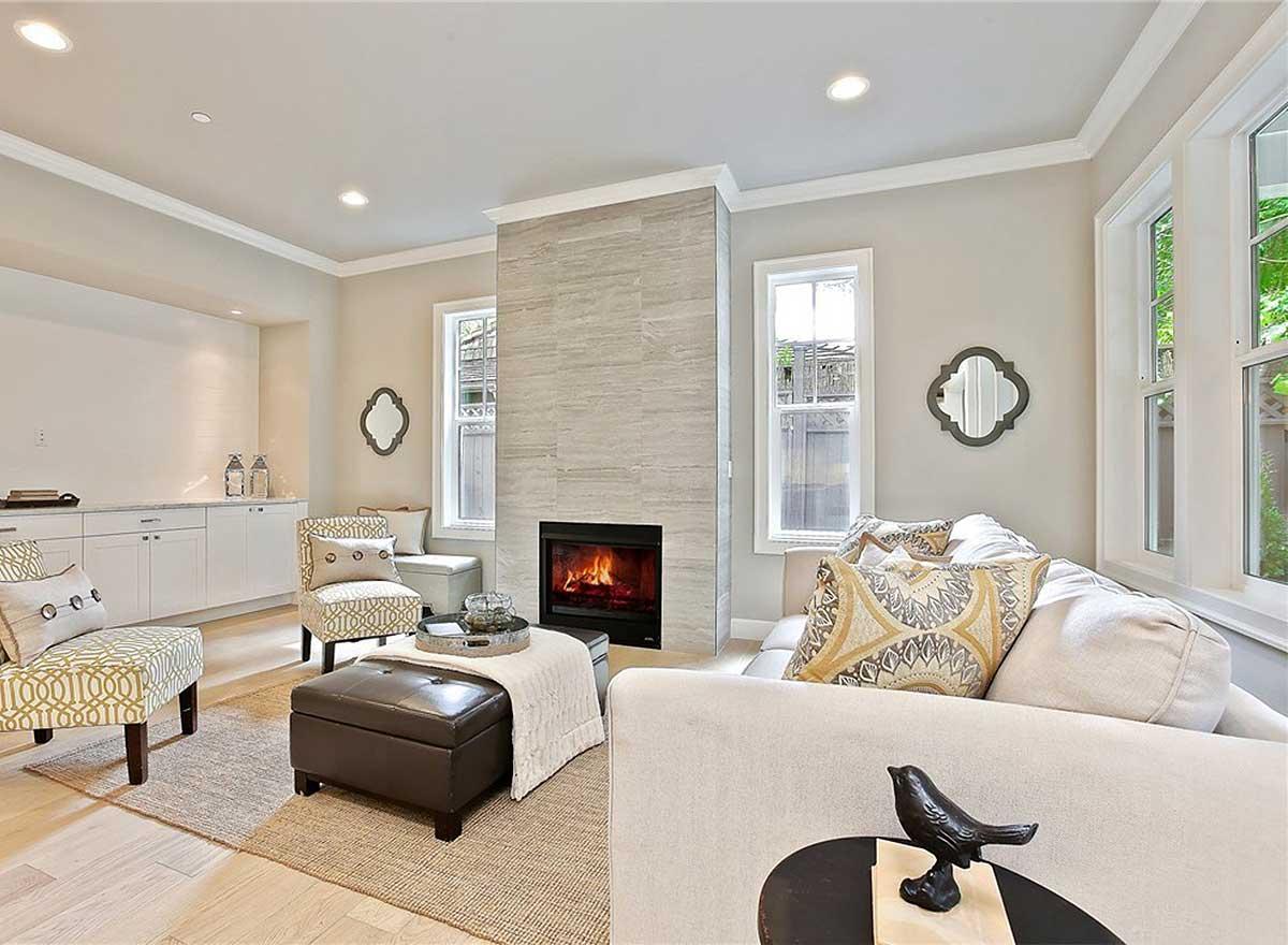 Living room with tiled fireplace, built-in cabinets, patterned armchairs, ottoman, and sectional sofa.