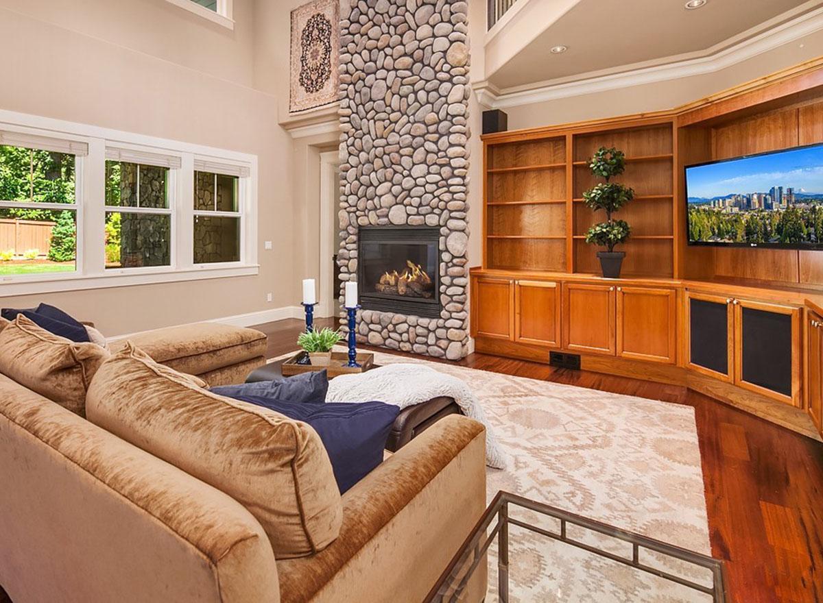 Great room with a floor-to-ceiling stone fireplace, built-in wood cabinetry, and large windows overlooking a backyard.