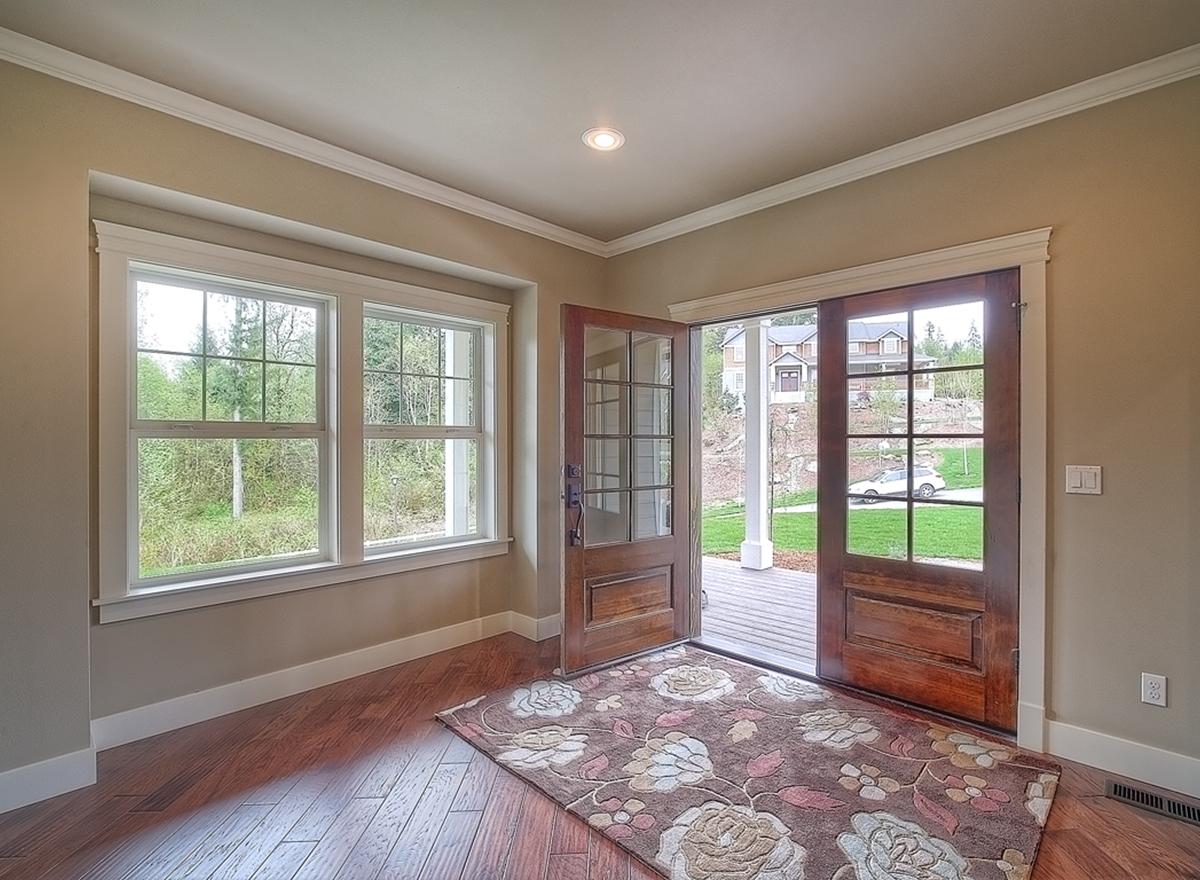Interior view of a house entrance with double wooden doors, a large window, and a deck with houses visible outside.