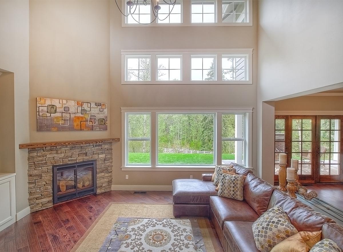 Interior view of a great room with a floor-to-ceiling stone fireplace, large windows, and an open layout.