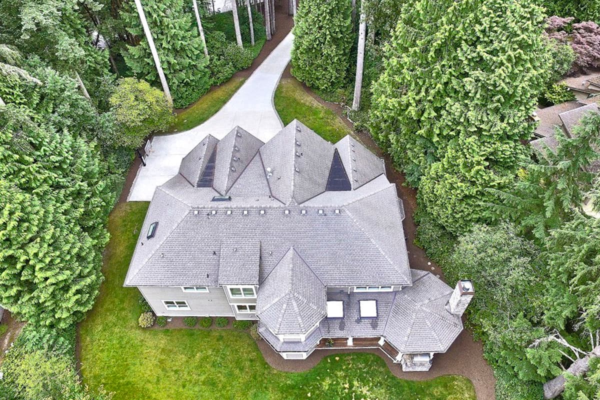 House plan exterior showing multiple gables, complex rooflines, a stone chimney, and a winding driveway.
