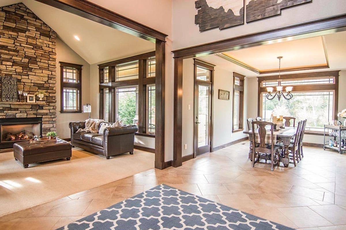 Living and dining area with stone fireplace, vaulted ceiling, large windows, and dark wood trim.