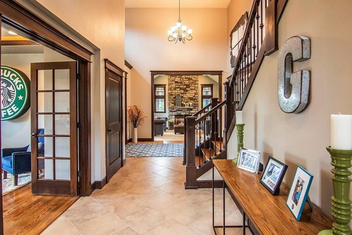 House interior foyer with dark wood staircase, stone fireplace visible, and tiled flooring.