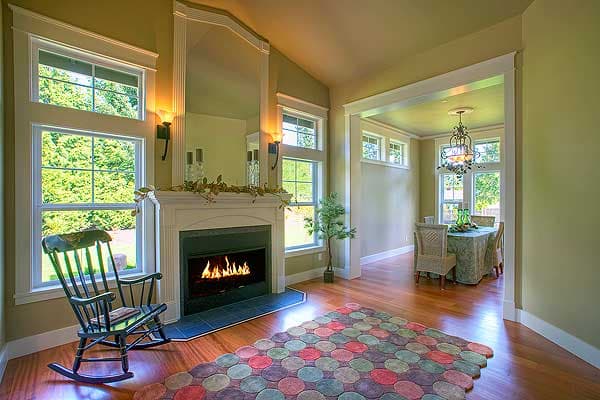 Living room with fireplace, rocking chair, and view of dining area. High windows with mullions throughout.