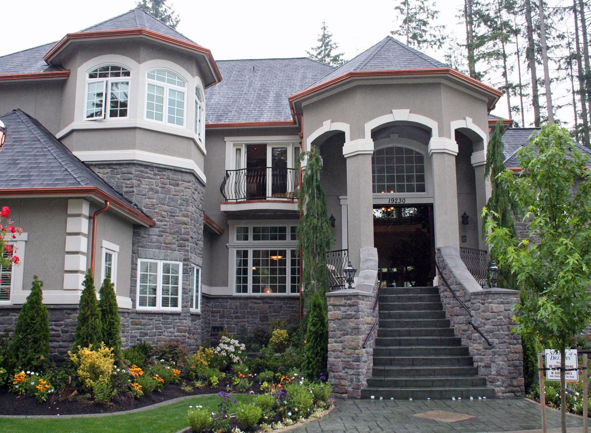 House plan exterior: Two-story home with stone accents, arched windows, and a grand stone staircase leading to the entrance.