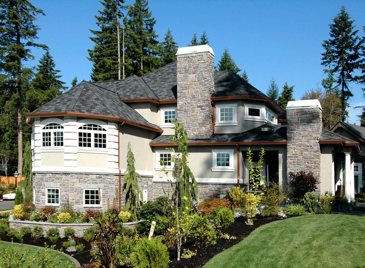 House plan exterior view of multi-story home with stone base, arched window bays, gable rooflines, and stone chimneys.