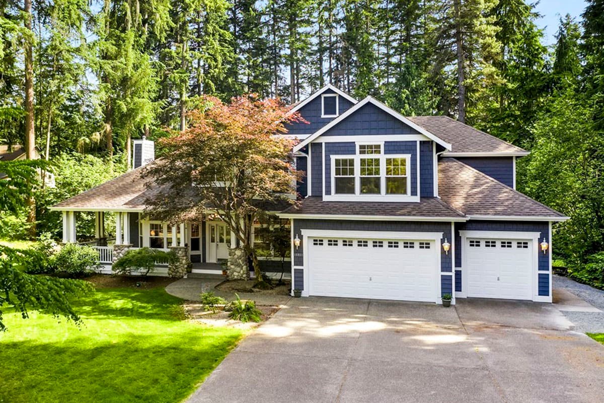 House plan exterior: Two-story blue house with a wrap-around porch, gables, dormers, and a three-car garage.