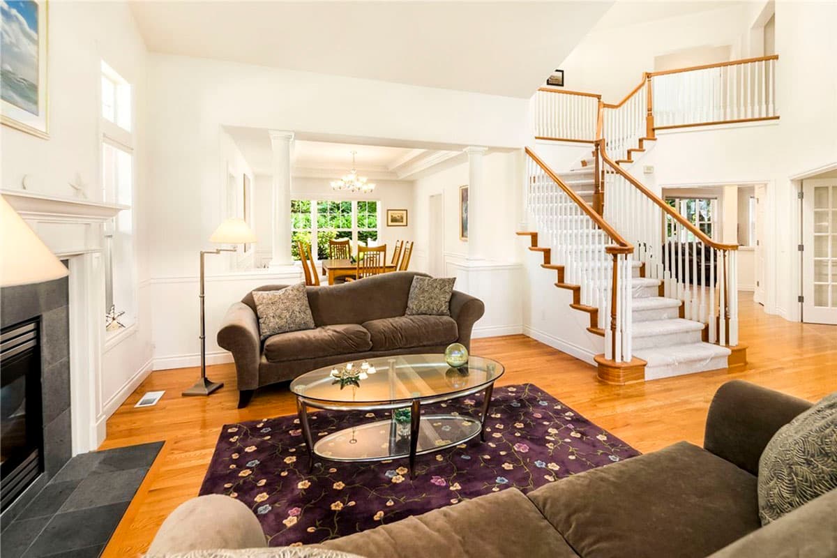 Interior view of a house interior showing a living room with fireplace, dining area, and a prominent staircase.