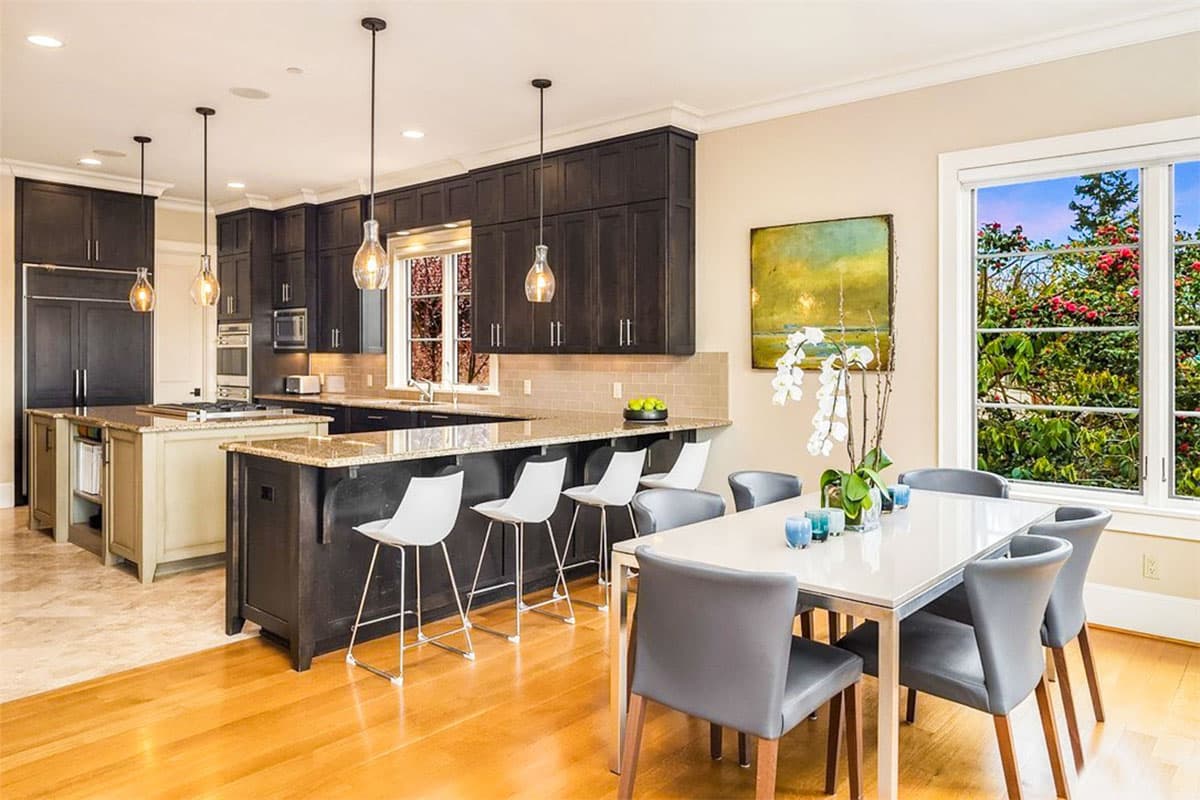 Kitchen with two islands, dark cabinetry, granite countertops, pendant lighting, and adjacent dining area with large windows.