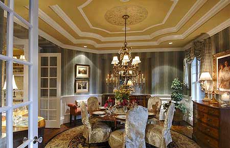 Formal dining room with a tiered tray ceiling, ornate chandelier, upholstered chairs, and a round dining table set for dinner.
