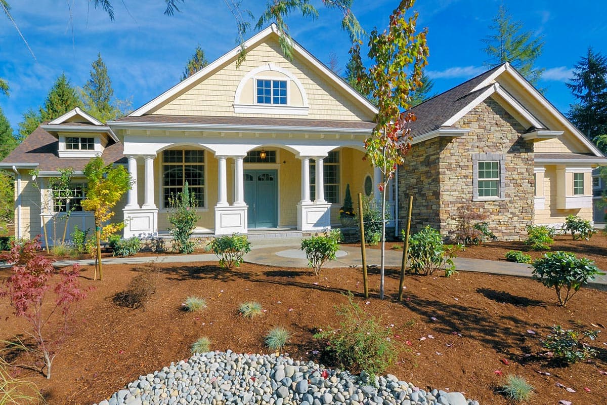 House plan exterior: one-story home with arched gable window, covered front porch with columns, and stone exterior accents.