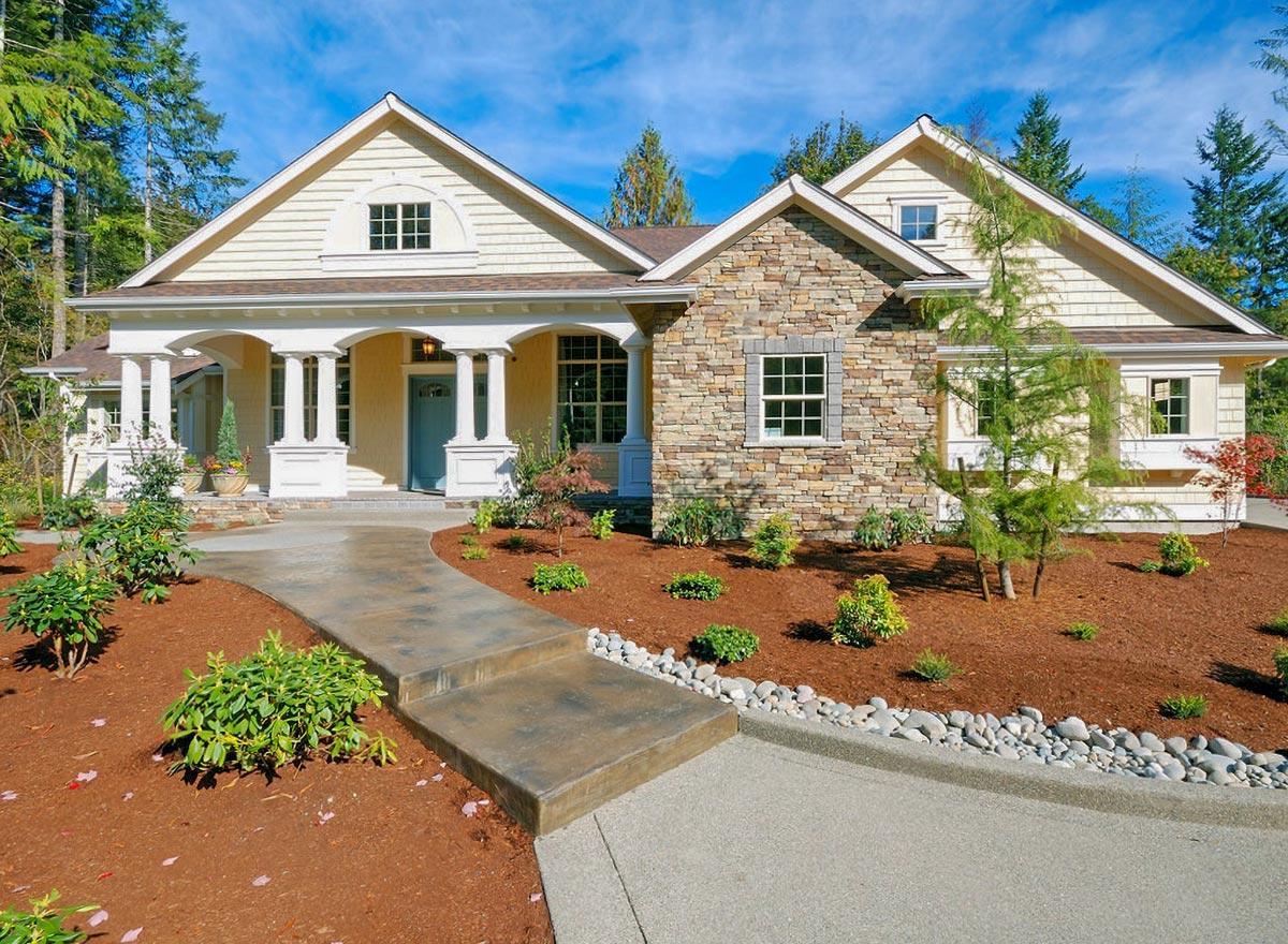 House plan exterior. Craftsman style, single-story home with a gabled roof, stone veneer, and a covered porch with pillars.