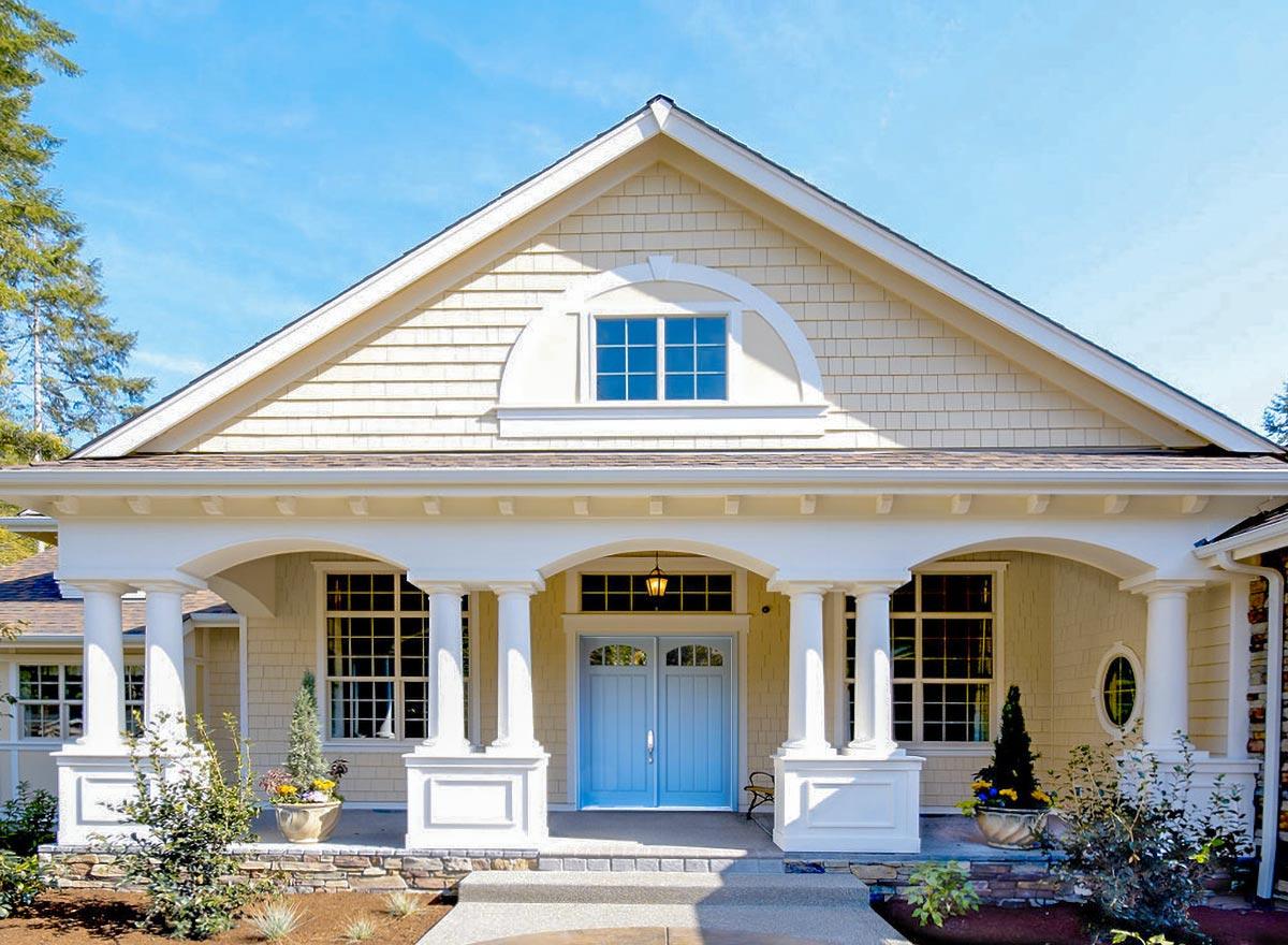 House plan exterior featuring a covered front porch with columns, arched openings, double blue doors, and a decorative arched dormer.