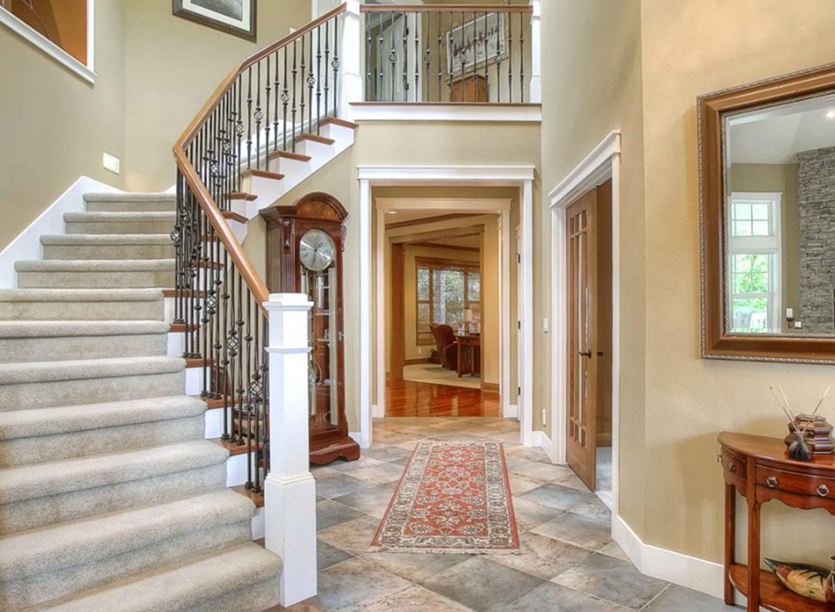 Foyer with curved staircase, grandfather clock, tiled floor, and doorway to living room.