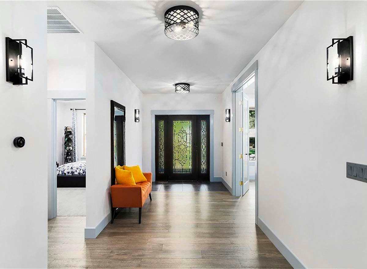 Interior view of a hallway with a glass-paneled front door, decorative ceiling lights, sconces, and an orange bench with yellow cushions.