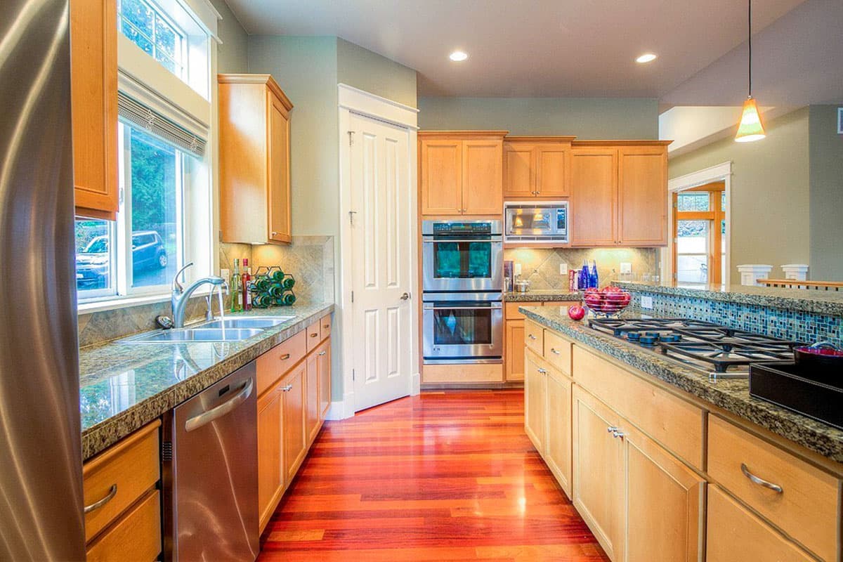 Kitchen with wood cabinets, granite countertops, gas range on island, double ovens, stainless steel appliances, and hardwood floors.