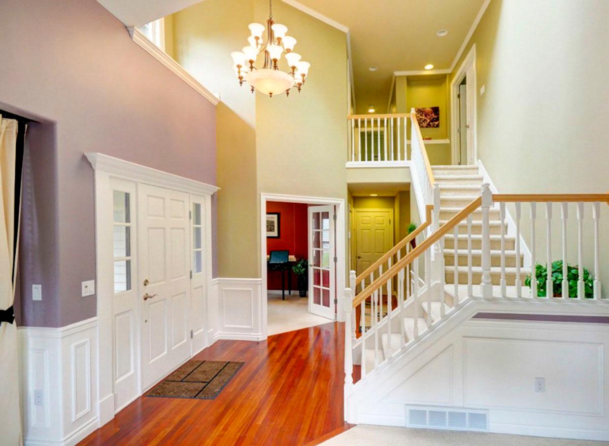 Interior view of a foyer with double entry doors, a grand staircase with white balusters and wood railings, and a chandelier.