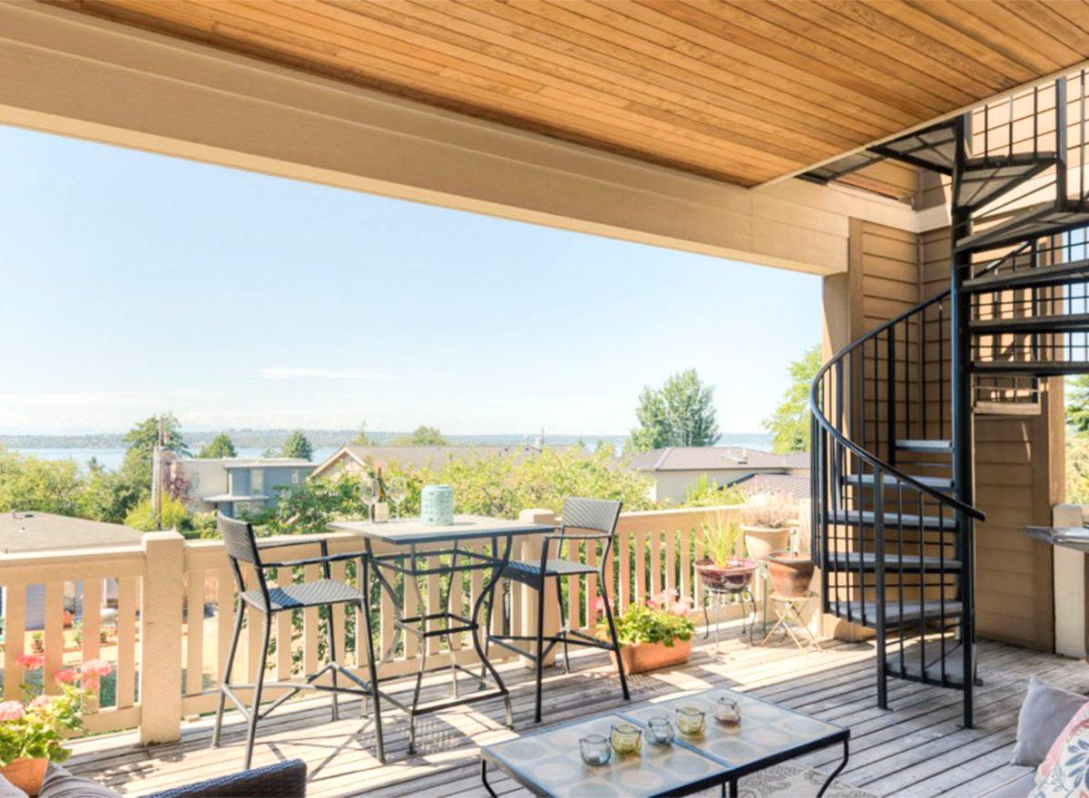 Covered deck with wood ceiling, bar seating, and spiral staircase, overlooking a residential area and water view.