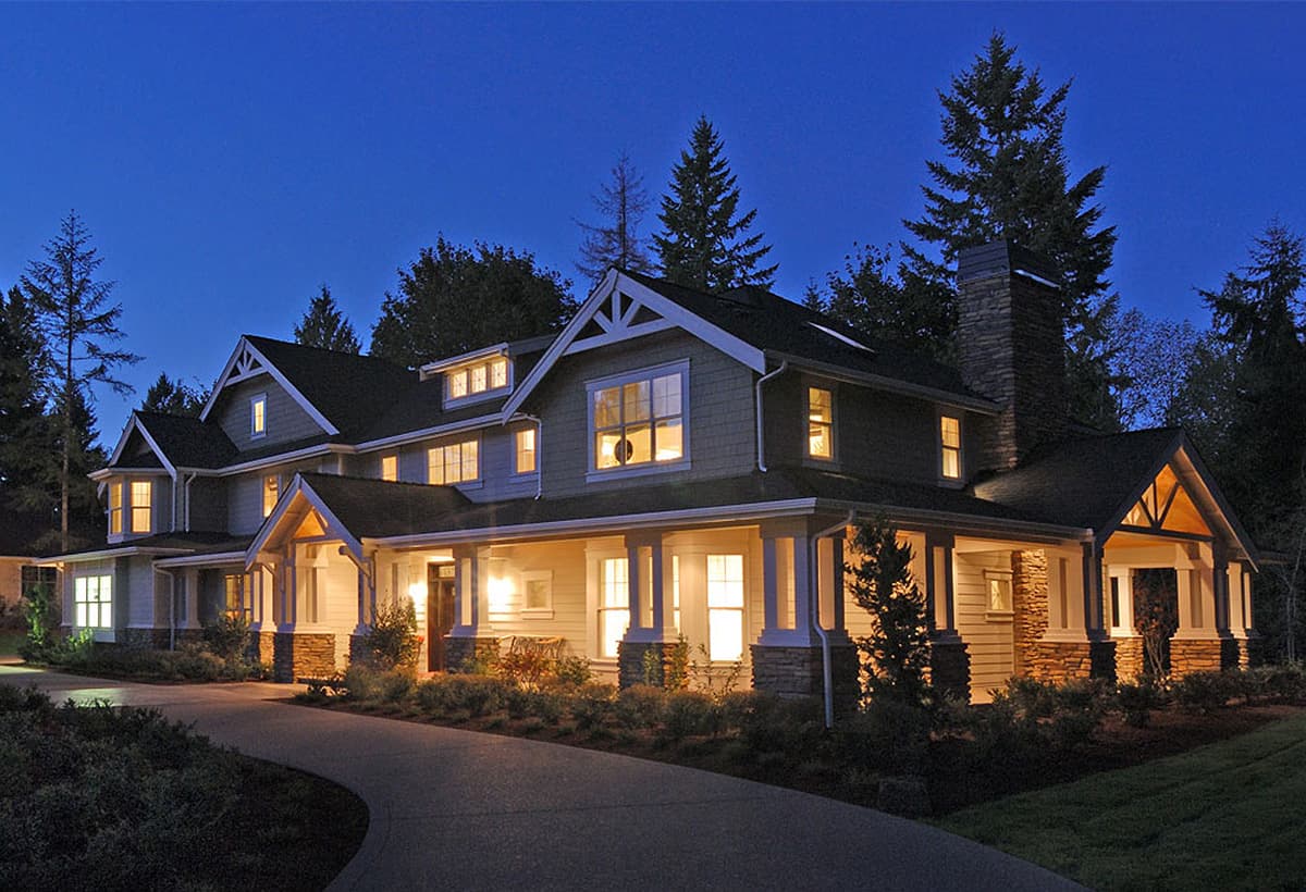 Craftsman style house plan exterior with a wraparound porch, multiple gables, dormer windows, and a stone chimney.